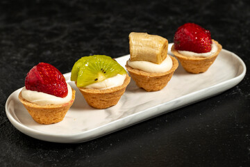 Fruit tartlet. Strawberry, kiwi and banana tartlet on a dark background. close up