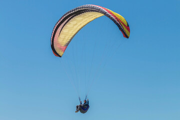 Multi-colored paraglider against the blue sky. Tandem flight.