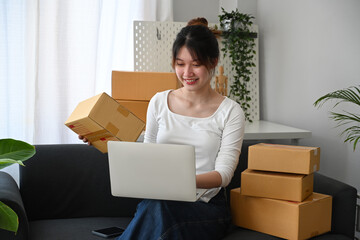 Smiling young woman online seller checking product purchase order on laptop computer. E-Commerce, online business, online sales concept