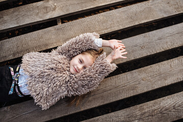 Portrait of a happy little girl lying on a wooden background. Beautiful baby enjoys a walk in the park. Fashionable children.