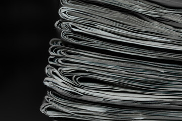 Detail shot of a pile of newspapers stacked on a table. Very out of focus background, library shelves.