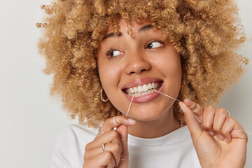 Close up shot of lovely European woman uses dental floss cleans teeth undergoes hygiene routines...
