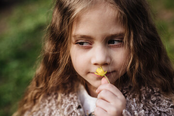 Cute baby enjoys the smell of a yellow plucked flower. Portrait of a beautiful girl holding flowers