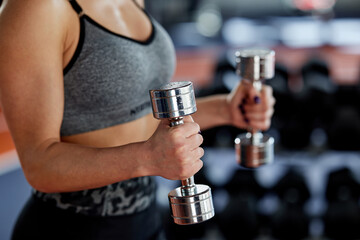 A fit, strong female bodybuilder is lifting dumbbells and doing exercises for biceps in a gym.