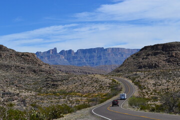 Eine Straße mit zwei Autos schlängelt sich durch die Berge und Wüste mitten im Big Bend National Park in Texas, Vereinigte Staaten von Amerika.