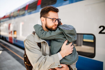 A father hugs his son at the train station before he goes to work.