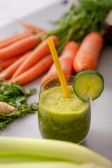 Green smoothie in glass with straw and cucumber and vegetagbles at background, detox, vegan, vegetarian healthy vegetable drink