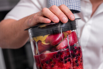 Close up cropped shot of man making smoothie from fresh fruits and berries in professional blender...