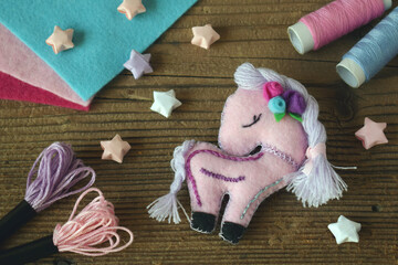 Making pink unicorn decored with purple and pink flower. Sewing from felt with your own hands. DIY concept for children. Handmade crafts.