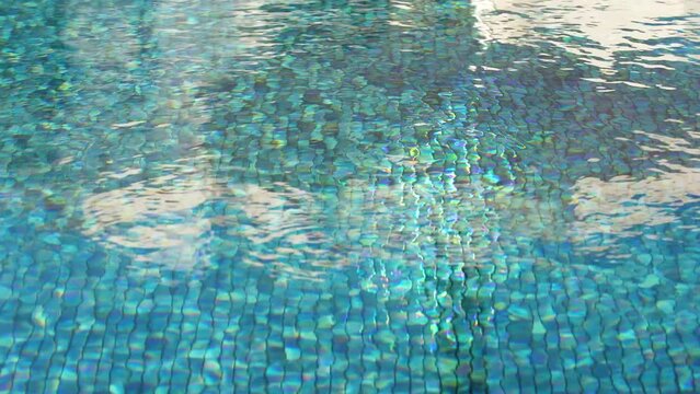Blue sunny bottom of swimming pool transparents through rippling flowing waves of clean transparent fresh water. Summer natural background. 4k stock video footage of texture of water surface