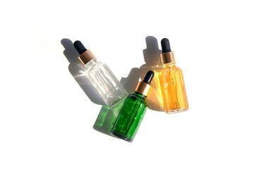 three glass bottles with pipettes with beautiful sun shadows, cosmetics of different types on a...