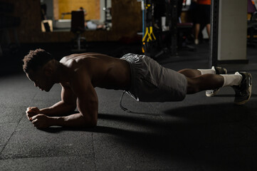Fototapeta na wymiar Shirtless african american man doing an elbow plank in the gym.