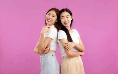 Studio portrait of Two asian woman in white t-shirt posing isolated on pink wall background. LGBT pride month concept.