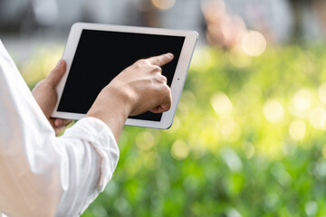 close up of hand holding tablet at outdoor green background 