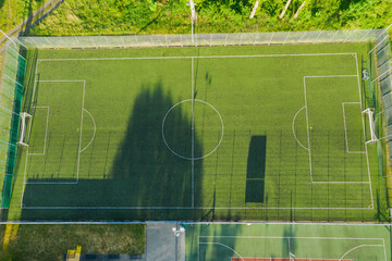 Prowincjonalny stadion. W centrum porośnięte murawą boisko piłkarskie, wokół bieżnia i niewielka trybuna dla kibiców. Widok z drona.