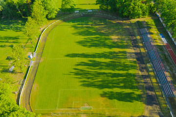 Fototapeta Prowincjonalny stadion. W centrum porośnięte murawą boisko piłkarskie, wokół bieżnia i niewielka trybuna dla kibiców. Widok z drona. obraz
