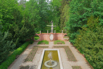 Park dworski w mieście Iłowa w zachodniej Polsce. Widać parkową fontannę, alejkę i mur ceglany zwany bramą księżycową. Widok z drona.