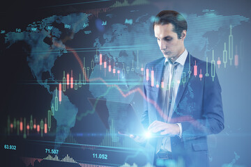 Attractive young european businessman using laptop with glowing forex chart hologram on blurry background. Finance, trade and fintech concept. Double exposure.