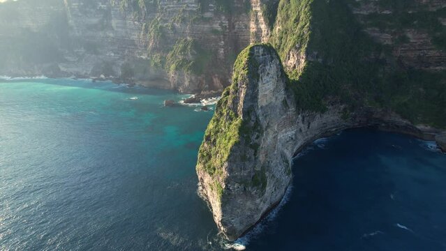 An aerial backwards drone shot of a cliffside of the tropical island of Nusapenida in the background. High quality 4k footage