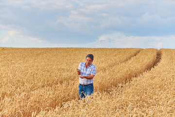 Happy farmer proudly standing in wheat field. Agronomist wearing corporate uniform, looking at camera on farmland.