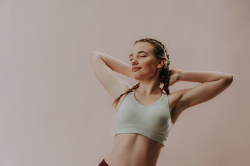 Young sporty woman in sports clothes with eyes closed meditating against beige background, copy space