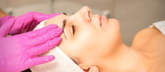 Cosmetologist with gloved hands applies a moisturizing mask with peeling cream on the female face....
