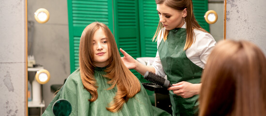 Fototapeta na wymiar Professional hair care. Young female red-haired with long hair receiving hairstyling in a beauty salon.