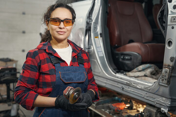 Fototapeta na wymiar Female auto mechanic with grinder tool standing in garage