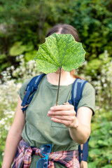 Young woman holding a green burdock leaf in her hand in front of her face in forest faceless anonymous psychological concept mockup