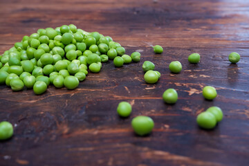 Fresh peeled green pease on a brown wooden table with copy space. Still life of green peas in pods with pea shoots on wooden table