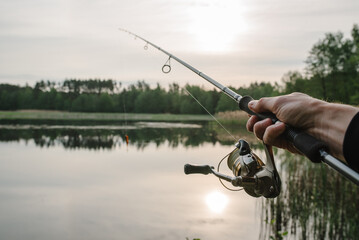 Fisherman with rod, spinning reel on the river bank. Sunrise. Fishing for pike, perch, carp. Fog against the backdrop of lake. background Misty morning. wild nature. The concept of a rural getaway.