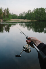 Fishing day. Fishing for pike, and perch from a lake, river or pond. Background wild nature. Fisherman with rod, spinning reel catches fish from a pier or boat. Article about concept of rural getaway.
