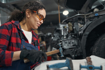 Female auto mechanic using hammer in car repair garage