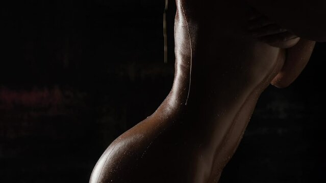 Beautiful tanned body close-up on a black background. Milk is poured on the girl's body close-up.