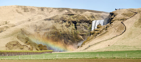 Skogar, Iceland, April 24, 2022: view across the field towards the Skogass waterfall with a rainbow...