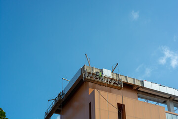 Using a construction gondola lift, workers place panels on a towering skyscraper. Building construction with blue sky as background © itsuky