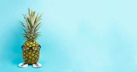 Pineapple with glasses and flip flops, vacation and travel concept, tropical summer holiday, funny fruit, blue background
