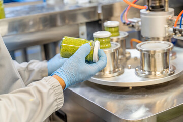 Pesto sauce Industrial process. High quality sauce production. Factory worker working on vacuum sealing machine for canned food. Italian basil taste in Pesto sauce. Vacuum Seamer for Cylindrical Cans