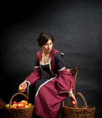 Girl in a medieval dress with a hood and a basket of apples. Historical costume.