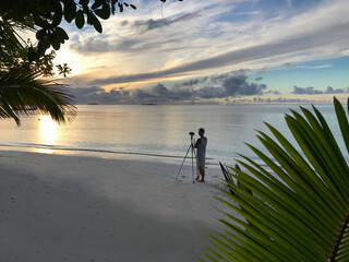 female photographer standing with camera and tripod to capture sunrise on the beach