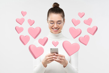 Smiling young woman using dating app on phone with hearts flying from screen as likes from men
