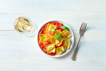 Ravioli with tomato sauce and fresh basil leaves on a plate, Italian pasta dish, shot from the top on a rustic wooden background with white wine