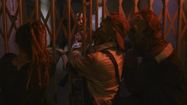 Military woman with shaved head standing in dark creepy building, looking at three zombies stuck behind metal gate of old elevator reaching their hands out