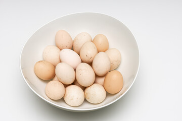 fresh unwashed rustic eggs lie in a deep bowl on a white background