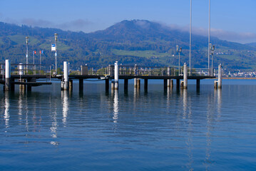 Fototapeta premium Scenic landscape with Lake Zürich and pier with flags seen from City of Rapperswil-Jona on a sunny spring day. Photo taken April 28th, 2022, Rapperswil-Jona, Switzerland.