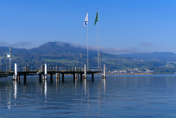 Scenic landscape with Lake Zürich and pier with flags seen from City of Rapperswil-Jona on a sunny spring day. Photo taken April 28th, 2022, Rapperswil-Jona, Switzerland.
