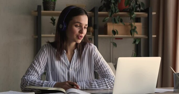Studying process use video call app, online tutoring concept. Young woman sit at desk improve language skills, make notes looking interested, wear headphones listen teacher enjoy easy comfort learning