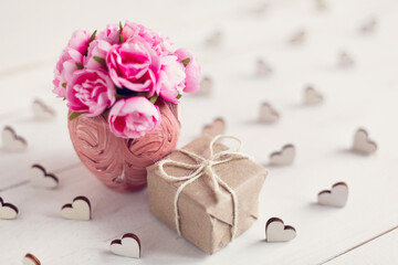 Little pink roses in a beautiful vase and a little gift wrapped in kraft paper.