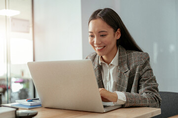 Close up of smiling Asian woman working at the office using a laptop sitting in meeting room