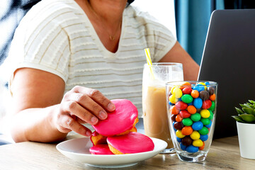 Overweight woman addicted to sweet eating sweet cake, candy hit calories drink while working...